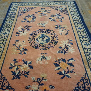 Pink rug featuring navy and gold floral motifs and complex borders on distressed wooden planks.