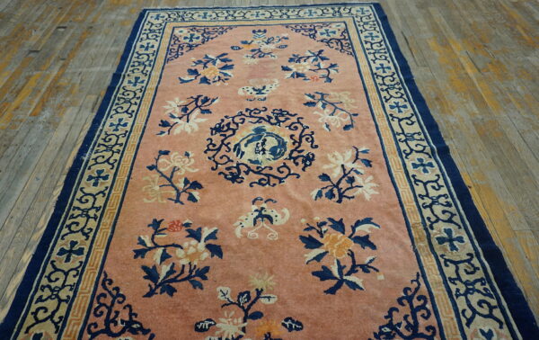 Pink rug featuring navy and gold floral motifs and complex borders on distressed wooden planks.