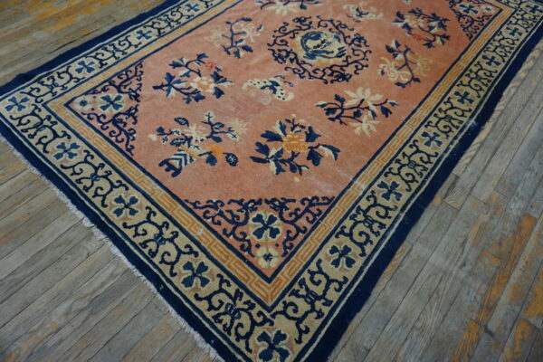 Worn peach rug with blue and cream floral motifs and geometric borders rests on diagonal wood planks.