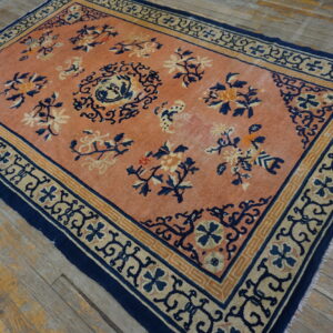 Low pile peach rug with navy blue floral patterns and geometric borders on distressed wood plank flooring.