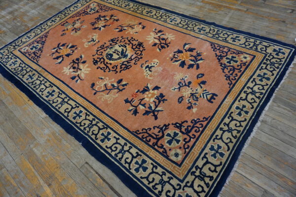 Low pile peach rug with navy blue floral patterns and geometric borders on distressed wood plank flooring.