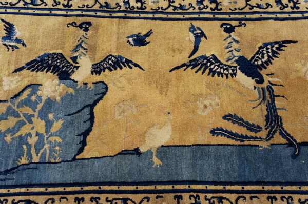 The rug has a tan field patterned with deep blue birds, rock formations, and elaborate blue borders.