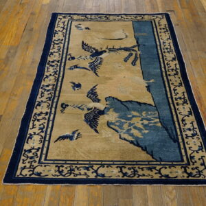 Low-pile tan and navy rug featuring flying bird and mountain designs, bordered by scrolling vines, lying on wood floors.