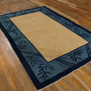 Beige and teal bordered rug with bamboo design rests on distressed wooden floorboards.