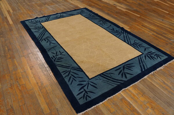 Beige and teal bordered rug with bamboo design rests on distressed wooden floorboards.