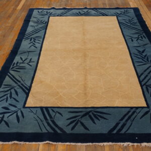 Beige rug with bamboo patterned blue border and fringe rests on light brown distressed wood floors.