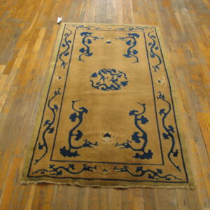 A golden tan rug with a navy blue stylized medallion and vine pattern rests on worn wood plank flooring.