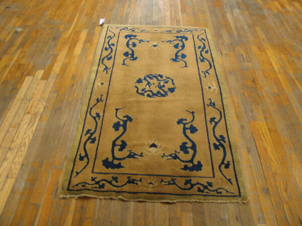 A golden tan rug with a navy blue stylized medallion and vine pattern rests on worn wood plank flooring.