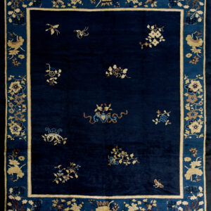 Plush navy rug with scattered floral and figural motifs, bordered in beige and blue on wood flooring.