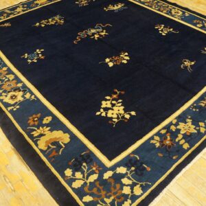 Navy blue rug with scattered gold floral sprays and a wide patterned border sits on light wooden flooring.