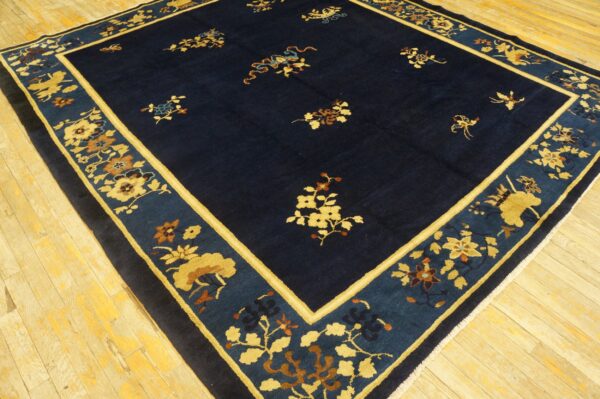 Navy blue rug with scattered gold floral sprays and a wide patterned border sits on light wooden flooring.