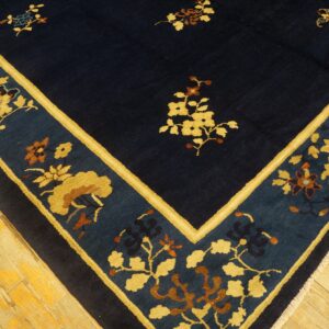 A dark blue floral rug featuring wide gold and teal borders rests on worn hardwood flooring.
