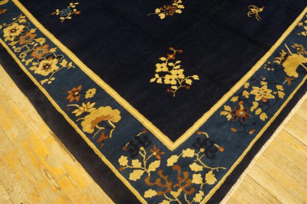 A dark blue floral rug featuring wide gold and teal borders rests on worn hardwood flooring.