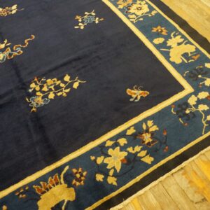 Dark blue rug with gold and rust floral motifs, bordered by teal and yellow, resting on wood plank flooring.