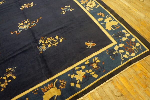 Dark blue rug with gold and rust floral motifs, bordered by teal and yellow, resting on wood plank flooring.