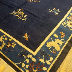 Dark blue rug with gold and teal floral patterns and wide borders rests on light wooden plank flooring.