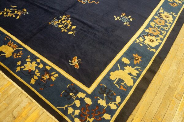 Dark blue rug with gold and teal floral patterns and wide borders rests on light wooden plank flooring.