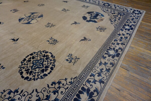Beige rug with traditional dark blue floral and greek key borders rests on distressed wood planks.