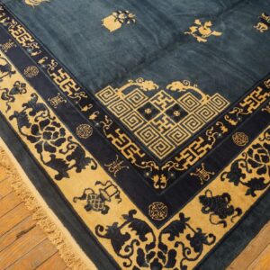 Low-pile rug in deep blue and gold with elaborate borders and fringe rests on rustic wood planks.