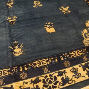 Navy blue rug with a gold floral pattern and intricate meander and scroll borders on a wood floor.