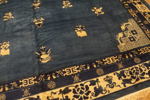 Navy blue rug with a gold floral pattern and intricate meander and scroll borders on a wood floor.