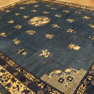 Large deep blue rug with scattered gold motifs and intricate multi-layered borders on wood floorboards.