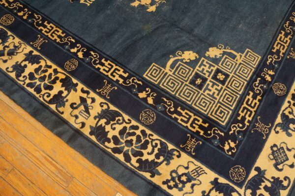 Dark blue rug border with elaborate gold key and floral motifs resting on light wood floorboards.
