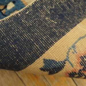 Detail of a rug showing the dark blue foundation and patterned beige pile edge over distressed wood flooring.