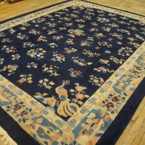 Dark blue rug features scattered multicolor floral and bird motifs and a wide beige decorative border on wood flooring.