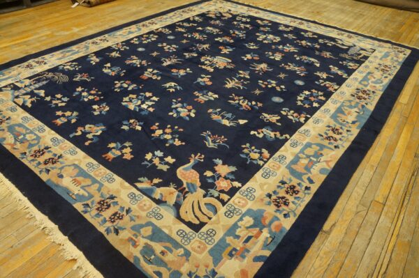 Dark blue rug features scattered multicolor floral and bird motifs and a wide beige decorative border on wood flooring.