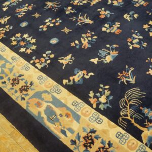 Navy rug with scattered floral designs and a wide cream, blue, and peach patterned border on wood floor.