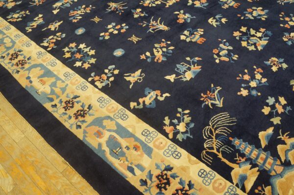 Navy rug with scattered floral designs and a wide cream, blue, and peach patterned border on wood floor.
