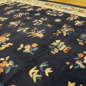Navy high-pile rug with colorful botanical designs and a wide tan border on a hardwood floor.
