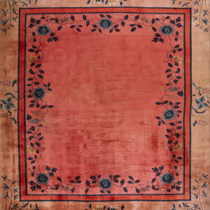 A pink and peach rug with a central field framed by dark blue floral and vine motifs.
