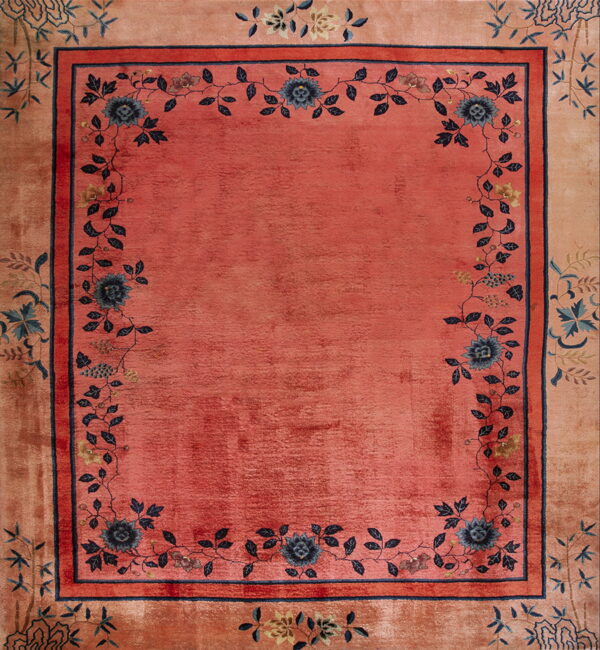 A pink and peach rug with a central field framed by dark blue floral and vine motifs.