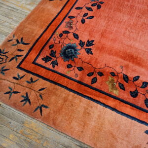 Coral-colored high-pile rug featuring a dark blue floral vine pattern on rustic wood floor.