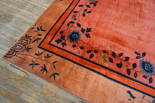 Coral-colored high-pile rug featuring a dark blue floral vine pattern on rustic wood floor.