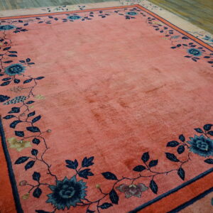 A coral rug with a wide blue floral vine border rests on distressed hardwood floors.