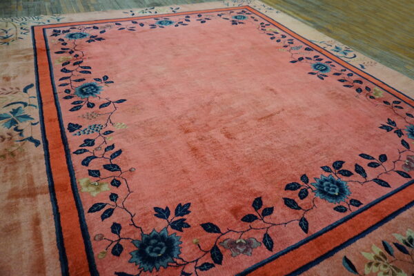 A coral rug with a wide blue floral vine border rests on distressed hardwood floors.