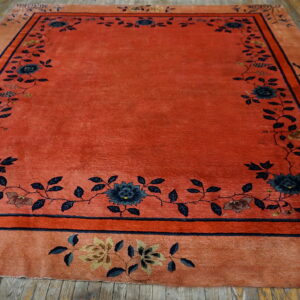 Red-orange rug with a dense navy floral border displayed on distressed wooden floorboards.