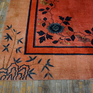 Coral and peach high-pile rug with navy floral and bamboo patterns rests on distressed yellow wood planks.