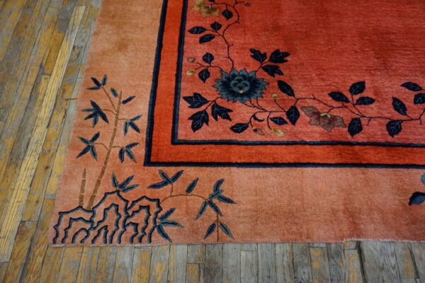 Coral and peach high-pile rug with navy floral and bamboo patterns rests on distressed yellow wood planks.