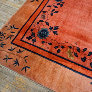Plush salmon rug with intricate navy blue floral borders rests on rustic wood planks.