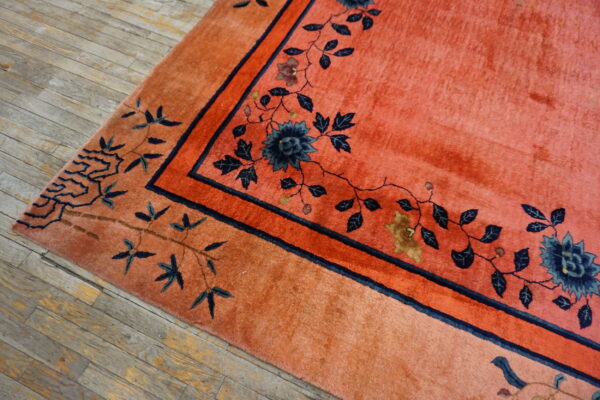 Plush salmon rug with intricate navy blue floral borders rests on rustic wood planks.