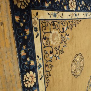 High-pile tan and navy rug featuring detailed floral borders rests on rustic, worn wooden floorboards.