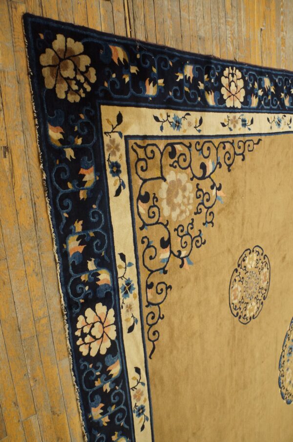 High-pile tan and navy rug featuring detailed floral borders rests on rustic, worn wooden floorboards.