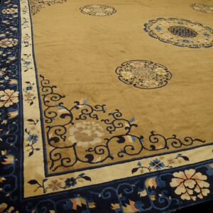 Angled view of a golden tan rug featuring navy blue medallions and a broad floral border.