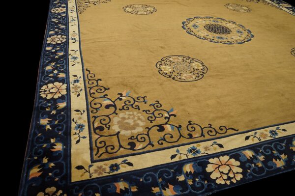 Angled view of a golden tan rug featuring navy blue medallions and a broad floral border.