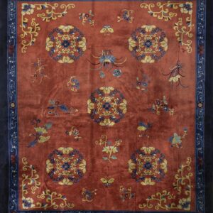 Reddish-orange rug with navy border, featuring yellow, blue, and burgundy stylized floral medallions.