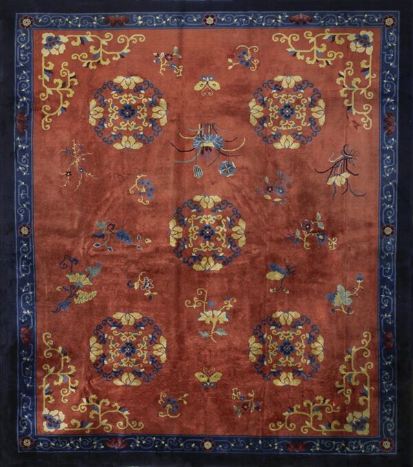 Reddish-orange rug with navy border, featuring yellow, blue, and burgundy stylized floral medallions.